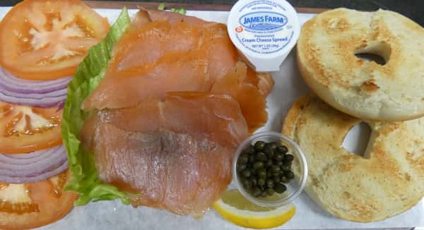 Toasted bagel with smoked salmon, cream cheese, capers, lettuce, tomato, red onion, and lemon wedge, served deconstructed.
