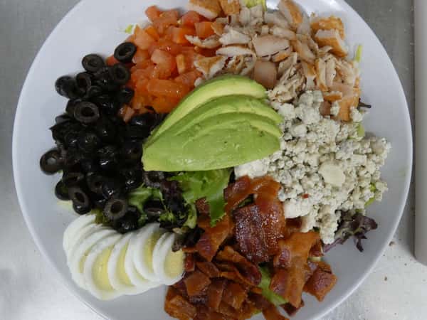 Classic Cobb salad with grilled chicken, bacon, avocado, hard-boiled egg, black olives, tomatoes, and blue cheese over mixed greens.