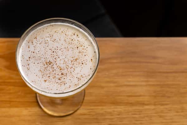 Overhead view of a creamy mezcal cocktail in a coupe glass, topped with a dusting of spices and served on a wooden bar at La Holly