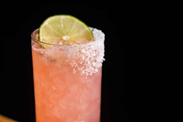Refreshing pink cocktail in a tall glass with crushed ice, coarse salt rim, and lime garnish, highlighting La Holly's vibrant mezcal drink menu