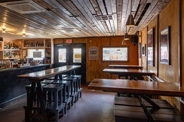Warm interior of La Holly cantina featuring rustic wood-paneled walls, a ceiling with exposed planks, modern pendant lighting, and a full bar with high-top seating.