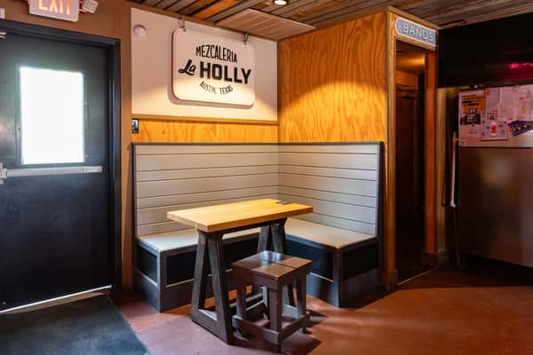 Cozy booth seating inside Mezcaleria La Holly in Austin, Texas, featuring light wood paneling, a minimalist table setup, and signage with a modern cantina vibe