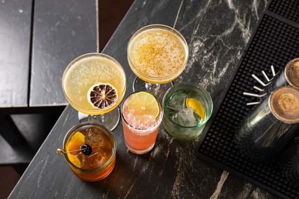 Overhead view of five artisanal cocktails at La Holly, featuring mezcal and tequila-based drinks with citrus garnishes, salt rims, and vibrant hues on a dark marble bar