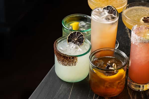 Assorted craft cocktails on a dark marble bar, featuring mezcal, tequila, and citrus-forward drinks in a mix of glass styles at La Holly