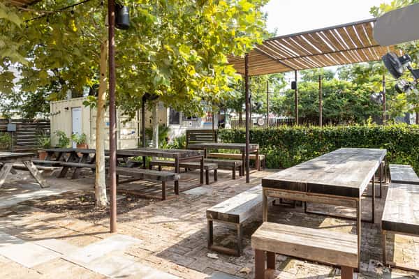 Alternate angle of La Holly's patio with rustic communal tables and bench seating under tree canopy and wooden slatted shade structure.