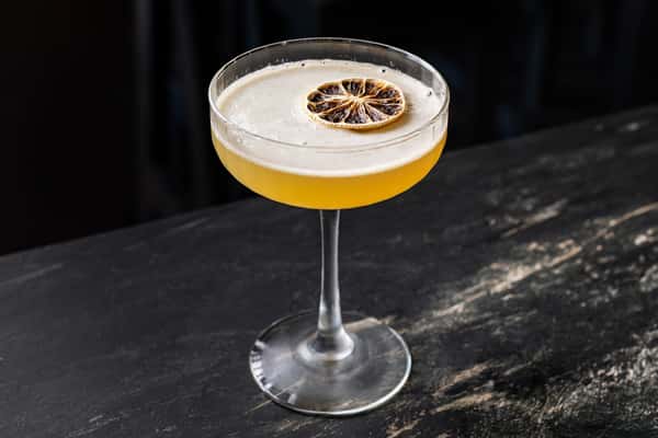 Elegant mezcal cocktail in a coupe glass with a burnt citrus garnish, showcasing its golden hue on a rustic dark bar surfac