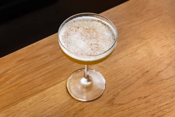 Mezcal cocktail in a coupe glass with a foamy top and spice garnish, presented on a warm wood bar in La Holly's stylish cantina