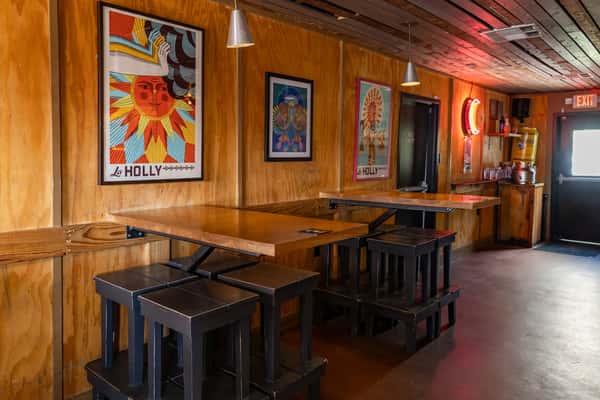Cozy indoor seating at La Holly with high-top wooden tables, modern pendant lights, and bold Latin-inspired wall art along wood-paneled walls.