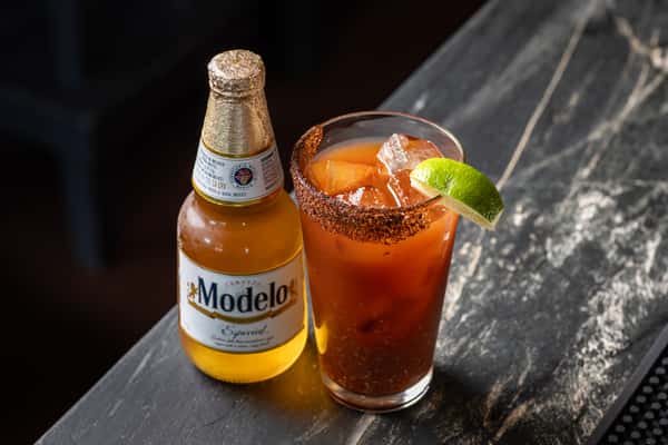 Michelada cocktail served with a bottle of Modelo Especial beer on a dark stone bar, garnished with a chili-lime rim and fresh lime wedge.