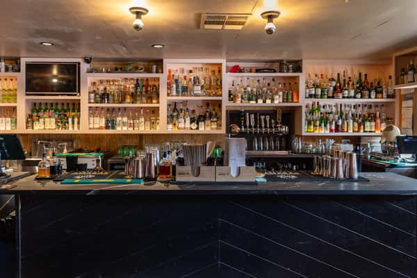 "Interior view of La Holly's bar in Austin, Texas, showcasing an extensive wall of mezcal and spirits, sleek black counter, and modern backlit shelving.