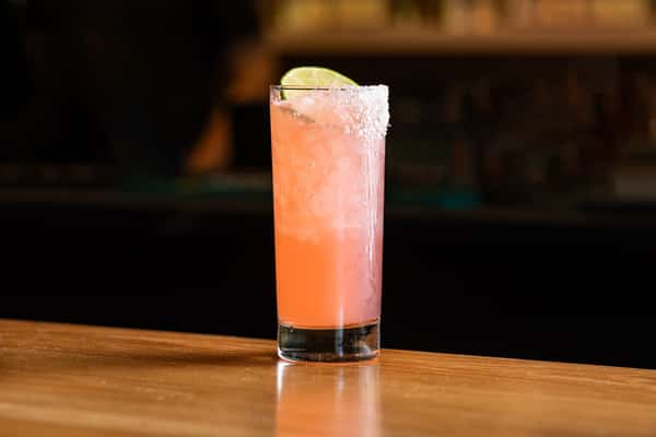 Vibrant grapefruit mezcal cocktail in a tall glass with a salt rim and lime garnish, set on a polished wooden bar in La Holly's cantina