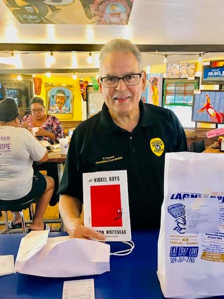 customer holding "Nickel Boys" book at Melba's restaurant table with takeout bags and community dining atmosphere