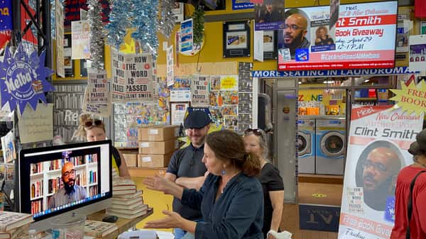 virtual author event at Melba's restaurant bookstore with guests watching live book talk on screen surrounded by community reading displays