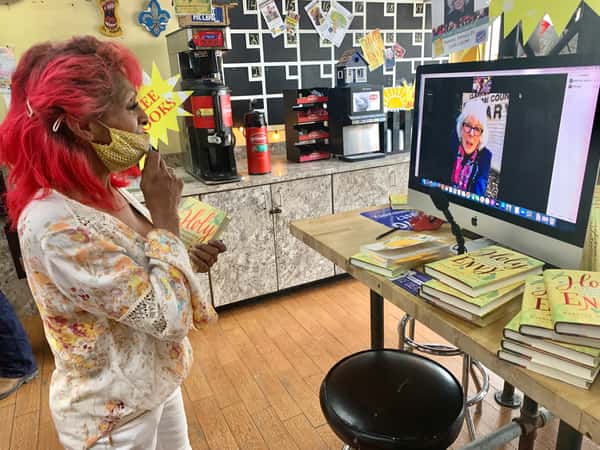 guest holding "Holy Envy" book while watching virtual author talk at Melba's New Orleans restaurant bookstore with cozy community vibe