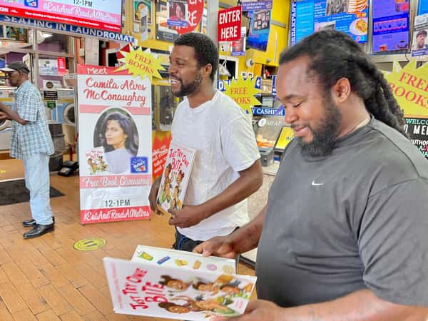 two guests holding books at Melba's restaurant during Camila Alves McConaughey book giveaway event with "Free Books" signs