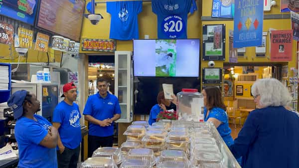 Melba's restaurant staff and guests gathered near takeout counter with Southern comfort food trays and lively community setting
