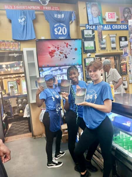 Melba's staff members holding books inside Southern restaurant near counter and menu boards during community literacy event