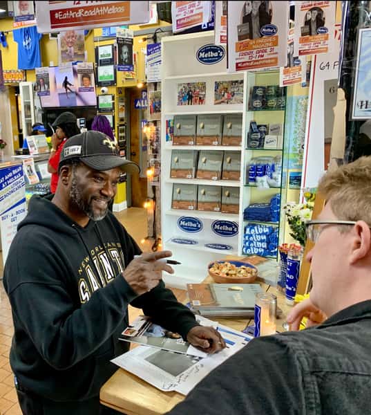 author signing books for guest at Melba's New Orleans restaurant table with merchandise display and community event atmosphere