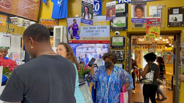 busy interior of Melba's Southern restaurant with customers ordering at the counter, colorful community posters, and book signing event signage on the walls