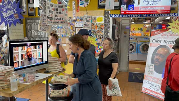 virtual author talk at Melba's restaurant bookstore with guests watching live reading on screen surrounded by "Free Books" displays