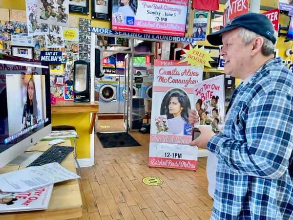 guest holding children's book while watching virtual author talk at Melba's restaurant bookstore with event signage in background