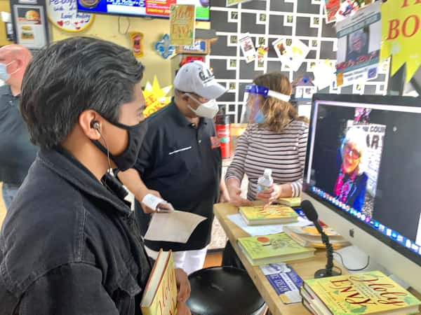 guests wearing masks watching virtual author reading at Melba's bookstore counter with stacks of books and event setup