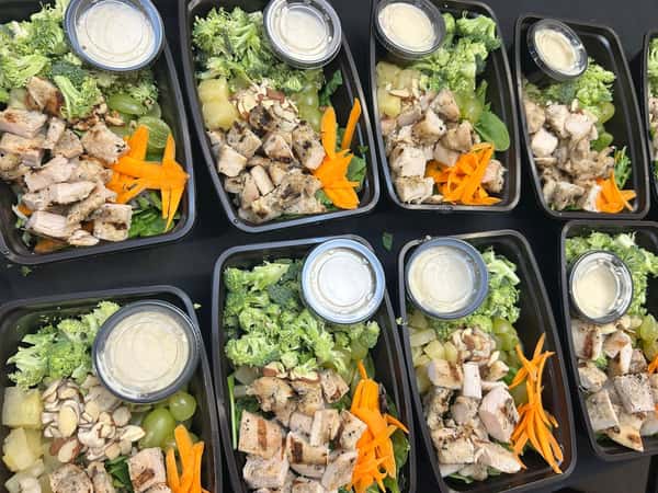 Grilled chicken meal prep bowls with fresh broccoli, grapes, pineapple, carrot ribbons, and sliced almonds with creamy dressing.