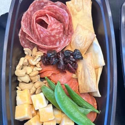 Tray with a salami rose, cheddar cubes, snap peas, dried cranberries, crackers, cashews, and pepperoni slices.