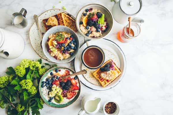 Colorful breakfast spread with waffles, porridge, fresh berries, kiwi, and pomegranate seeds served on a marble surface.
