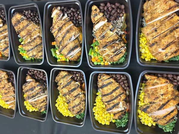 Grilled chicken breast meal prep with corn, black beans, and mixed vegetables in black containers.