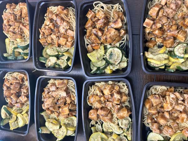 Meal prep trays with teriyaki chicken over noodles, served with sautéed zucchini and yellow squash on a dark wood table.