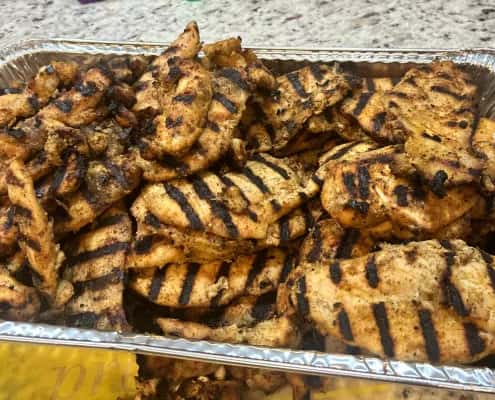 Tray filled with grilled chicken breasts marked with dark sear lines on a kitchen countertop.