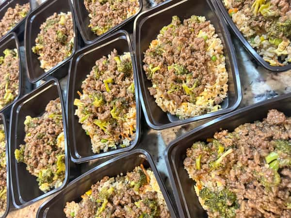 Ground beef and broccoli stir fry over fried rice in black meal prep containers.