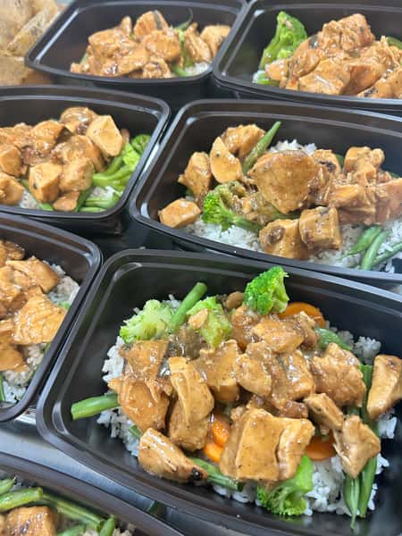 Meal prep containers filled with grilled chicken, white rice, broccoli, green beans, and carrots in a savory sauce.