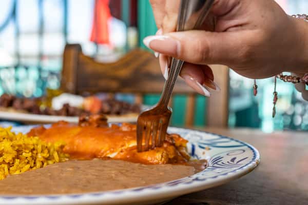 Woman holding up a bit of an enchilada with a fork with a cheese pull paired with beans and rice