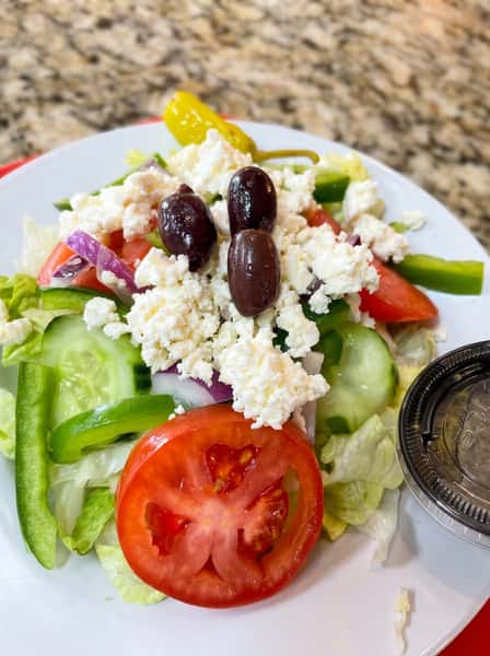 Greek salad with lettuce, tomatoes, cucumbers, bell peppers, red onion, feta cheese, olives, and a pepperoncini.