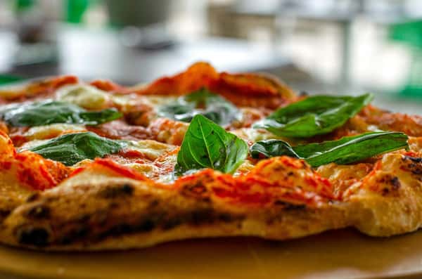Close-up shot of fresh basil leaves topping a classic Italian pizza with melted cheese and tomato sauce.