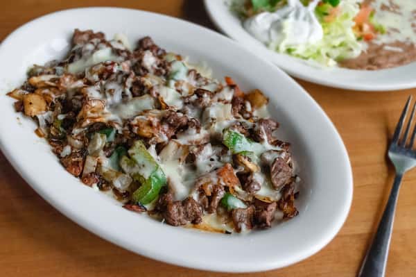 Grilled steak with sautéed onions and peppers topped with melted cheese, served with rice, beans, and salad on a white plate.