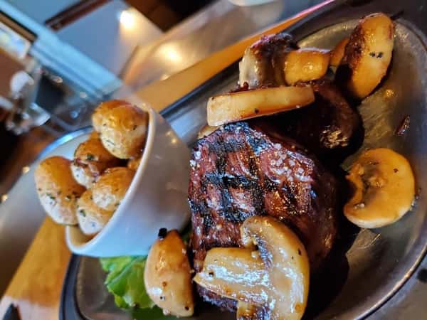 Two 4 ounce medallions of beef marinated in a burgundy peppercorn sauce with thick cut mushrooms with butter roasted potatoes.
