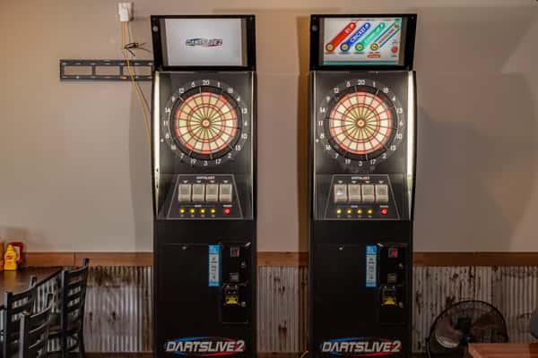 Two electronic dart machines, DARTSLIVE2, positioned side by side inside a restaurant with seating nearby.