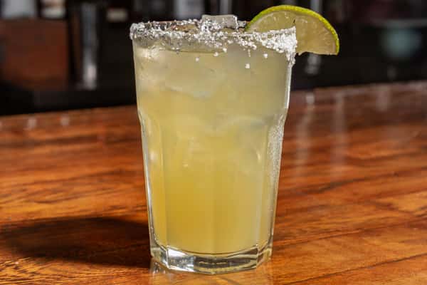 Classic margarita on the rocks with salted rim and lime wedge garnish served in a tall glass.