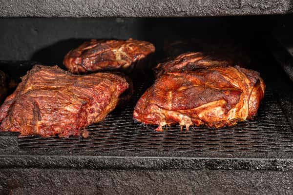 Smoked barbecue pork shoulders cooking inside a smoker with a dark charred crust forming.