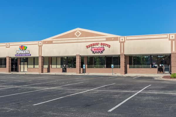 Exterior view of Rubbin' Butts BBQ restaurant next to Popaleta Ice Cream Snacks in a strip mall with an empty parking lot.