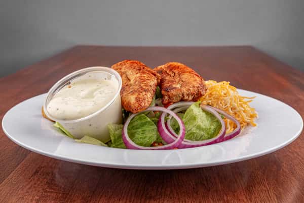 Grilled chicken salad with shredded cheese, red onion, lettuce, and ranch dressing served on a white plate.