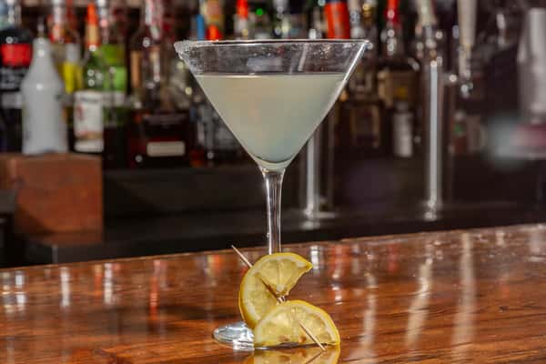 Martini glass with a lemon cocktail, sugar rim, and lemon slices on toothpicks garnish, set on a wooden bar counter.