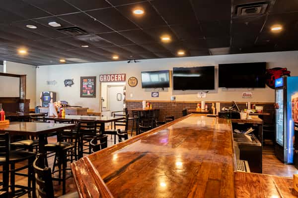 Interior of Rubbin' Butts BBQ featuring wooden tables, chairs, a long polished bar, wall-mounted TVs, and rustic decor.