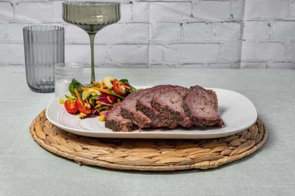 Sliced smoked beef brisket seasoned with a peppery rub, plated alongside a vibrant garden salad with cherry tomatoes and corn—ideal for a Texas barbecue entrée or upscale BBQ presentation.