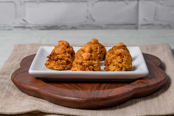 Golden mini crab cakes topped with spicy aioli, served on a white rectangular plate over a wooden board—ideal for Southern-inspired appetizers or coastal catering menus.
