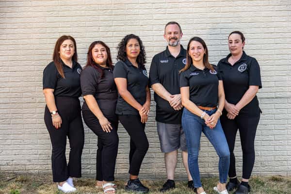 Group portrait of a restaurant staff team standing in front of a brick wall, all wearing branded black uniforms—highlighting professionalism and team spirit in a local dining establishment.