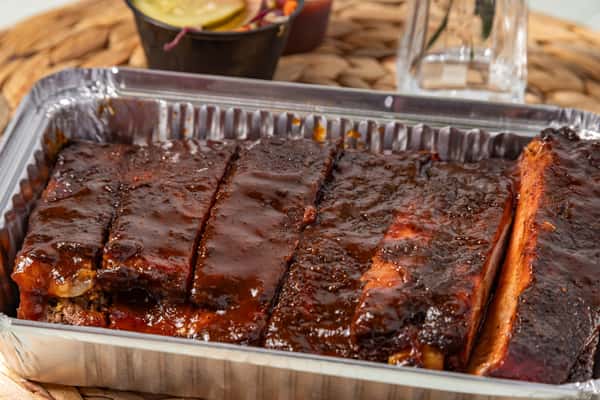 Close-up of saucy BBQ pork ribs in a foil container, glazed with a rich barbecue sauce—ideal for takeout menus or Southern-style catering services.